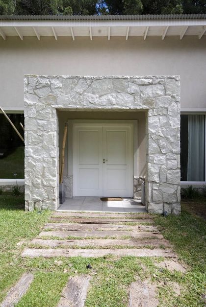 Entrada moderna con fachada de piedra y doble puerta blanca — proyecto Casa Cariló 2007, por Hugo Zawadski Arquitectos, en Cariló