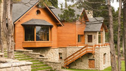 Fachada rústica moderna de madera y piedra en bosque — proyecto Corrientes del Nahuel, por Ricardo Pereyra Iraola , en Bariloche
