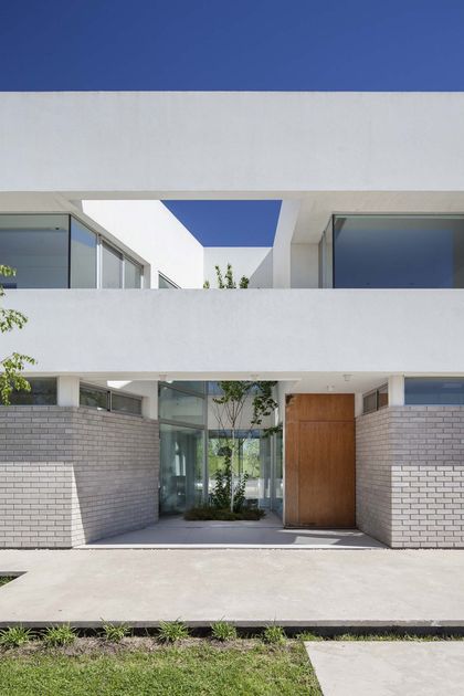 Fachada moderna blanca con entrada de madera y jardín interior — proyecto Casa MA, por Estudio GR, en City Bell