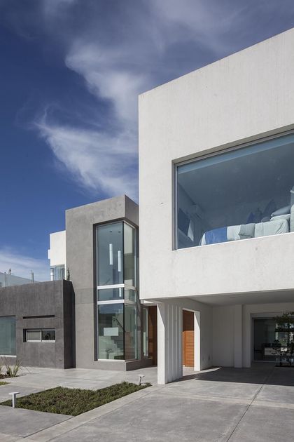 Fachada moderna de hormigón blanco y gris con grandes ventanales y escalera flotante — proyecto Casa FA, por Estudio GR, en City Bell