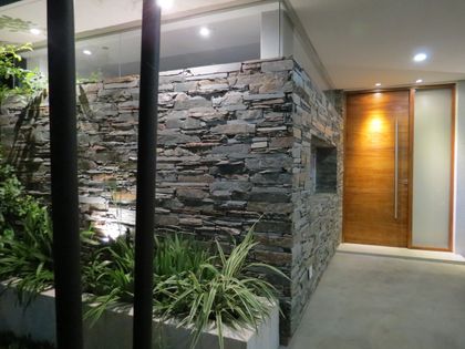 fachada moderna con piedra apilada y puerta de madera — proyecto Casa GT- Barrio Los Arenales, por Olivieri Arquitectura, en Ingeniero Maschwitz