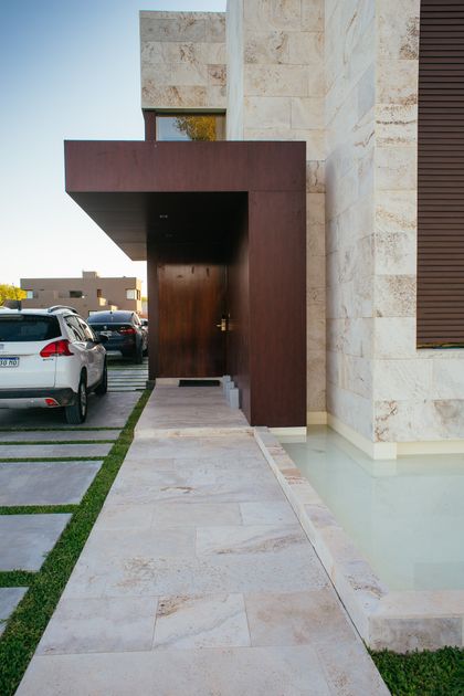fachada moderna con piedra, madera y agua — proyecto Grand Bell 60, por Mercedes  klappenbach, en City Bell