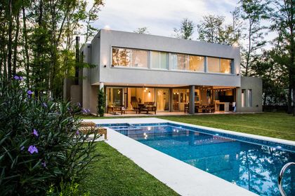 Casa moderna con pileta iluminada al atardecer entre árboles — proyecto Casa 18, por Parrado Arquitectura