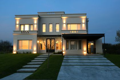 Casa contemporánea de dos plantas iluminada al atardecer con jardín delantero — proyecto Casa 17, por Parrado Arquitectura