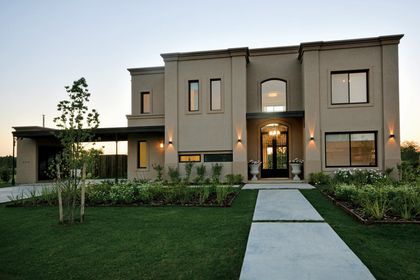 Casa contemporánea con fachada gris, iluminación nocturna y jardín frontal — proyecto Casa 15, por Parrado Arquitectura