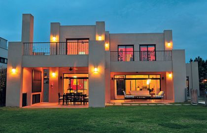 Casa contemporánea iluminada al atardecer con fachada gris y jardín verde — proyecto Casa 10, por Parrado Arquitectura