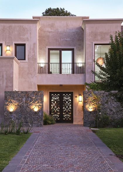 Fachada contemporánea rosa con puerta ornamental negra iluminada — proyecto SD 48, por Estudio Arq Daniel Tarrio
