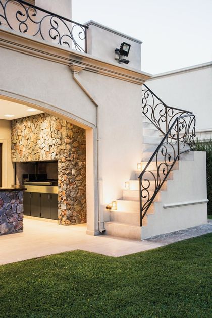 Casa contemporánea con escalera de hierro negro y fachada de piedra iluminada — proyecto TRV 164, por Estudio Arq Daniel Tarrio