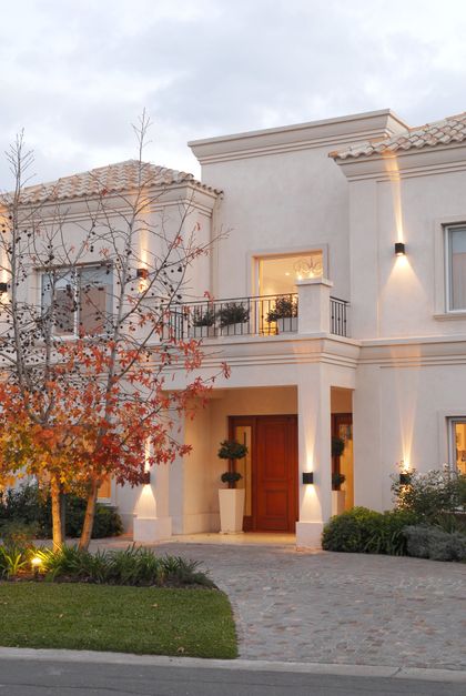 Casa blanca moderna con entrada roja al atardecer iluminada — proyecto VO 38, por Estudio Arq Daniel Tarrio
