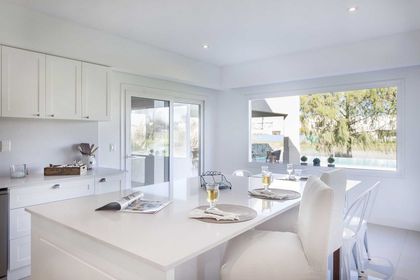 Cocina minimalista blanca con isla, mesada mármol y grandes ventanales — proyecto TRV 137, por Estudio Arq Daniel Tarrio