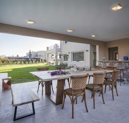 Amplio patio con comedor de madera, sillas de mimbre y jardín verde al fondo — proyecto TRV 137, por Estudio Arq Daniel Tarrio