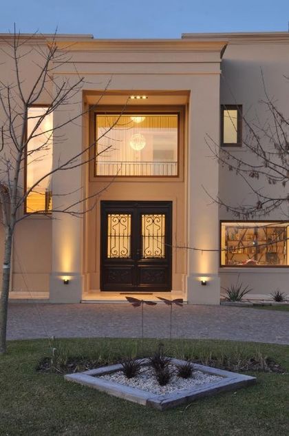 Fachada contemporánea iluminada con puerta negra y vidrieras doradas — proyecto TRV 195, por Estudio Arq Daniel Tarrio