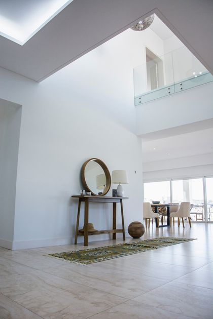 Hall doble altura minimalista con consola madera y espejo redondo — proyecto TRV 620, por Estudio Arq Daniel Tarrio