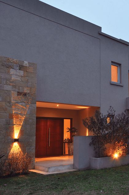 Fachada contemporánea gris con puerta roja iluminada y piedra vista — proyecto LP 149, por Estudio Arq Daniel Tarrio