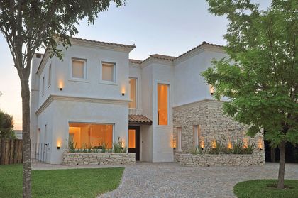 Casa moderna blanca y piedra con iluminación cálida al atardecer — proyecto LS 78, por Estudio Arq Daniel Tarrio