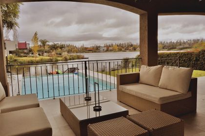 Terraza cubierta con sillones, vista a pileta y campo verde — proyecto Altamira del Lago, por Marconi Silva Arquitectos, en Tigre