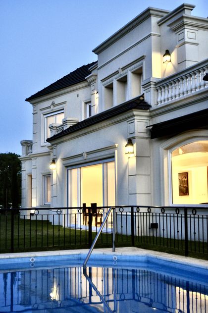 Mansión blanca contemporánea con pileta al atardecer, iluminada elegantemente — proyecto Ayres del Pilar, por Marconi Silva Arquitectos, en Pilar