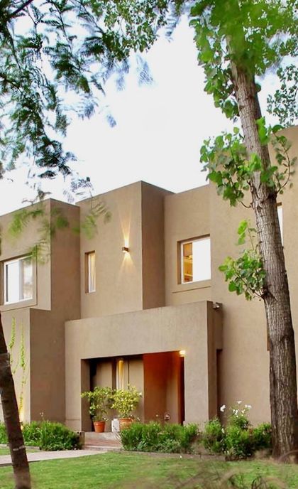 Casa contemporánea beige con fachada minimalista y árboles frondosos — proyecto El Encuentro  2, por Marconi Silva Arquitectos, en Benavidez