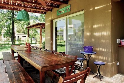 Galería rústica con mesa madera, pérgola y vista al jardín — proyecto El Encuentro  2, por Marconi Silva Arquitectos, en Benavidez