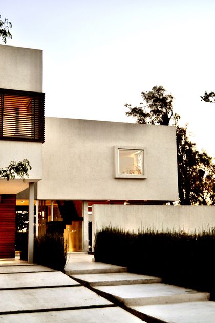 Fachada minimalista en hormigón con entrada roja y luminoso atardecer — proyecto Haras Santa María, por Marconi Silva Arquitectos, en Escobar