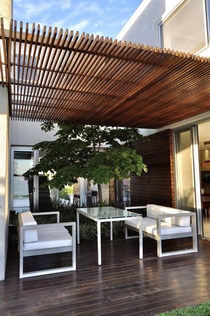 Terraza moderna con pergola de madera, muebles blancos y plantas verdes — proyecto Haras Santa María, por Marconi Silva Arquitectos, en Escobar