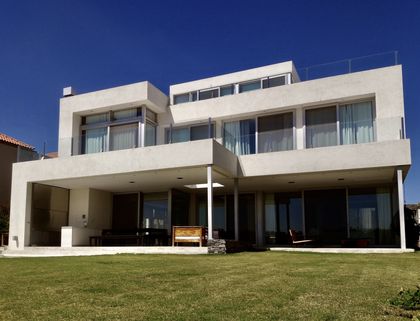 Casa moderna blanca con fachada limpia y amplio jardín céspedes — proyecto Lagos del Golf, por Marconi Silva Arquitectos, en Nordelta
