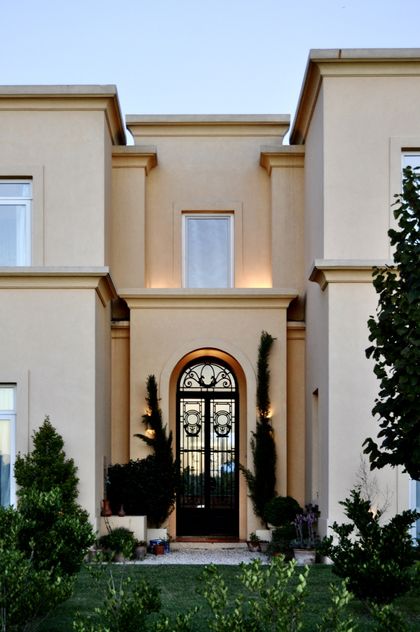 Fachada contemporanea beige con puerta arqueada negra y columnas — proyecto Lagos del Norte, por Marconi Silva Arquitectos, en Don Torcuato