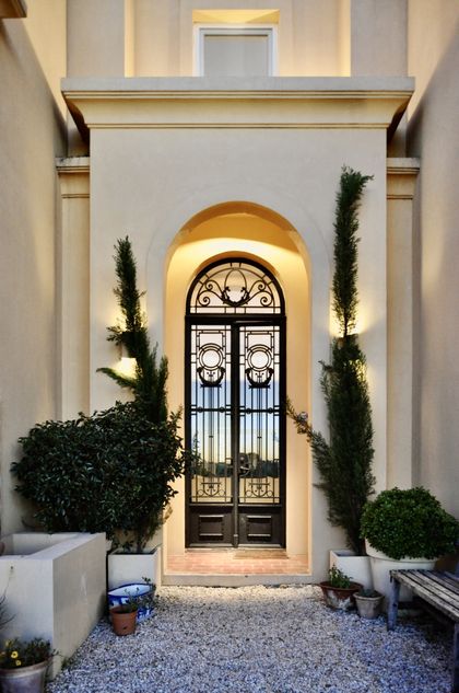 Entrada clásica con puerta ornamental, arco dorado y plantas ciprés — proyecto Lagos del Norte, por Marconi Silva Arquitectos, en Don Torcuato