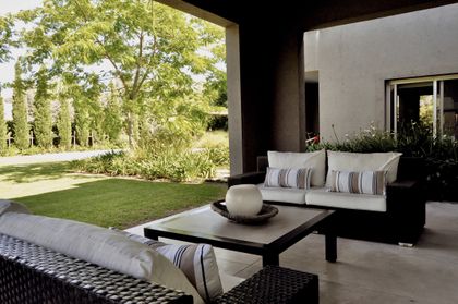 Terraza moderna con sillones tapizados y vistas al jardín arbolado — proyecto Martindale Country Club, por Marconi Silva Arquitectos, en Pilar