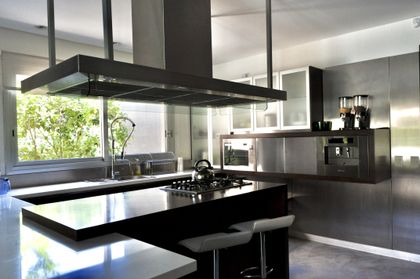 Cocina minimalista con isla negra y ventanal panorámico al jardín — proyecto Martindale Country Club, por Marconi Silva Arquitectos, en Pilar
