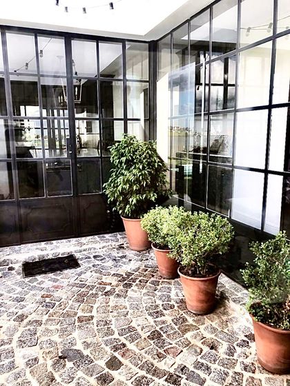Patio con adoquinado de piedra, grandes ventanales negros y plantas — proyecto San Matías, por Marconi Silva Arquitectos, en Belén de Escobar