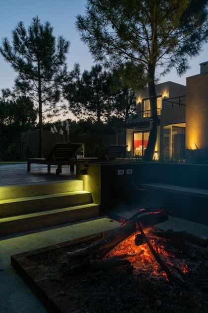 terraza moderna con fogonero, deck de madera e iluminación cálida — proyecto Costa Esmeralda 1, por Arquitecto Caceres, en Costa Esmeralda