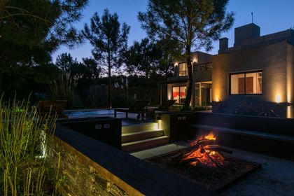 Living exterior moderno con fuego y vegetación de noche — proyecto Costa Esmeralda 1, por Arquitecto Caceres, en Costa Esmeralda