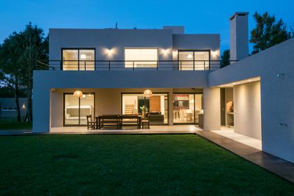 Fachada moderna de casa con patio y luces cálidas — proyecto Costa Esmeralda 2, por Arquitecto Caceres, en Costa Esmeralda
