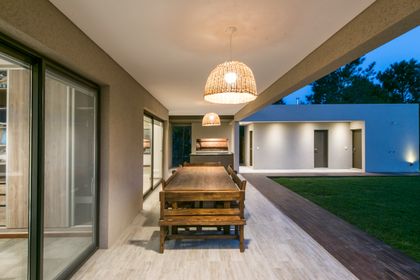 Comedor exterior bajo pérgola con luces tejidas y mesa de madera — proyecto Costa Esmeralda 2, por Arquitecto Caceres, en Costa Esmeralda