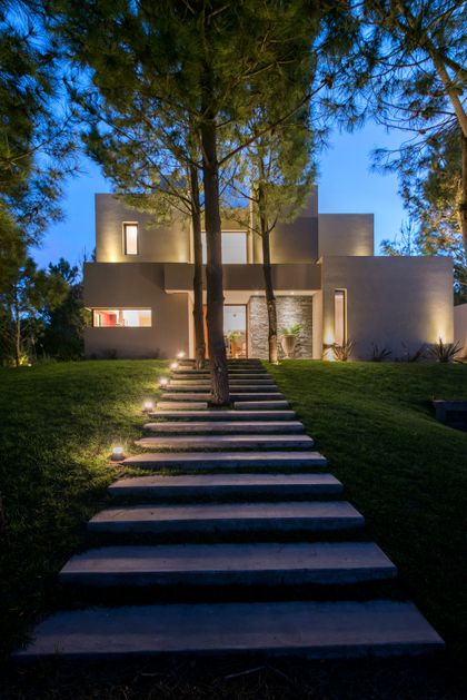 fachada moderna con escaleras flotantes y árboles iluminados — proyecto Costa Esmeralda 2, por Arquitecto Caceres, en Costa Esmeralda