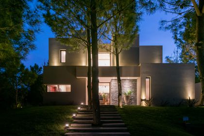 Fachada moderna de hormigón con iluminación nocturna e árboles — proyecto Costa Esmeralda 2, por Arquitecto Caceres, en Costa Esmeralda