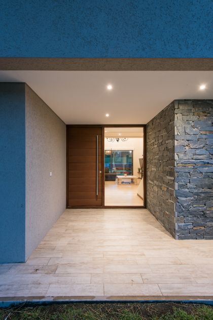 Entrada moderna con puerta pivotante de madera y revestimiento de piedra — proyecto Costa Esmeralda 2, por Arquitecto Caceres, en Costa Esmeralda