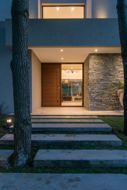 Fachada moderna con puerta de madera y muro de piedra — proyecto Costa Esmeralda 2, por Arquitecto Caceres, en Costa Esmeralda