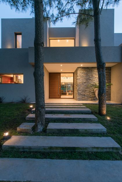 fachada moderna con camino de losas de hormigón y árboles — proyecto Costa Esmeralda 2, por Arquitecto Caceres, en Costa Esmeralda
