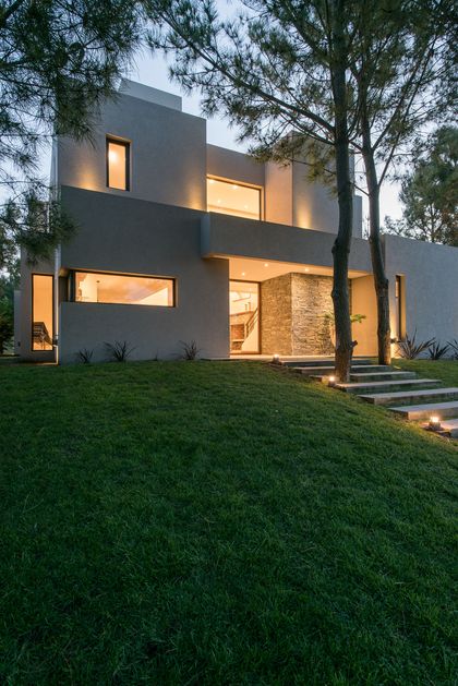 Fachada moderna gris con piedra y ventanas amplias en bosque — proyecto Costa Esmeralda 2, por Arquitecto Caceres, en Costa Esmeralda