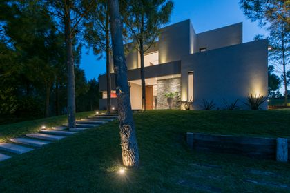 Fachada moderna blanca con iluminación cálida y jardín — proyecto Costa Esmeralda 2, por Arquitecto Caceres, en Costa Esmeralda