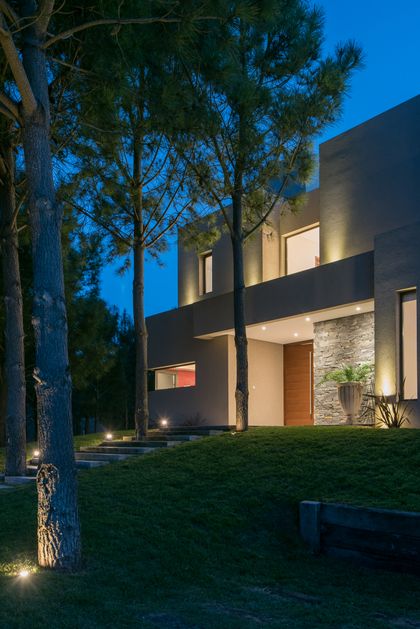 Fachada moderna iluminada con árboles y detalles en piedra — proyecto Costa Esmeralda 2, por Arquitecto Caceres, en Costa Esmeralda