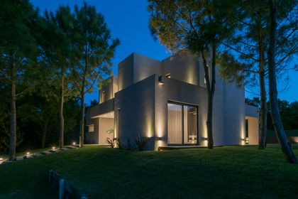 Fachada moderna iluminada con luces cálidas y rodeada de vegetación — proyecto Costa Esmeralda 2, por Arquitecto Caceres, en Costa Esmeralda