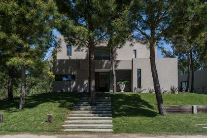 Fachada moderna de hormigón con amplios ventanales y vegetación — proyecto Costa Esmeralda 2, por Arquitecto Caceres, en Costa Esmeralda
