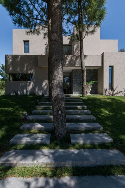 Fachada moderna con escalones de hormigón y árbol prominente — proyecto Costa Esmeralda 2, por Arquitecto Caceres, en Costa Esmeralda