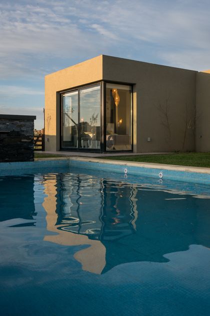 Piscina moderna con reflejos y casa minimalista — proyecto Costa Esmeralda 3, por Arquitecto Caceres, en Costa Esmeralda