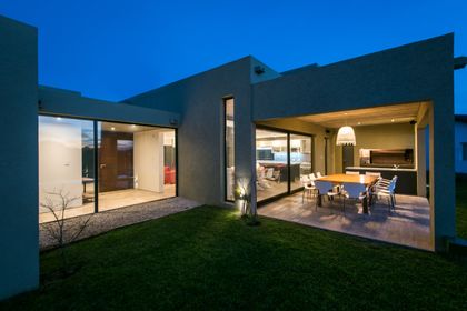 Fachada moderna blanca con luces cálidas y comedor exterior — proyecto Costa Esmeralda 3, por Arquitecto Caceres, en Costa Esmeralda