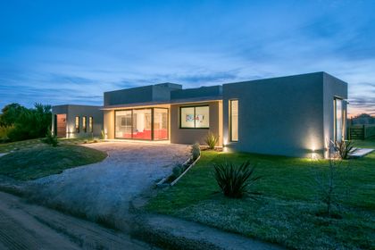 fachada moderna gris con grandes ventanales de noche — proyecto Costa Esmeralda 3, por Arquitecto Caceres, en Costa Esmeralda