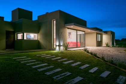 Fachada moderna con jardín y sala exterior al atardecer — proyecto Costa Esmeralda 3, por Arquitecto Caceres, en Costa Esmeralda